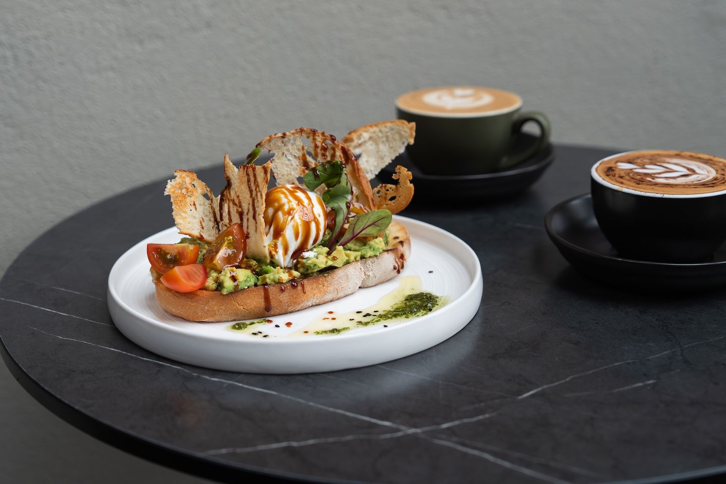 A sandwich on a white plate with a cup of coffee in the background.