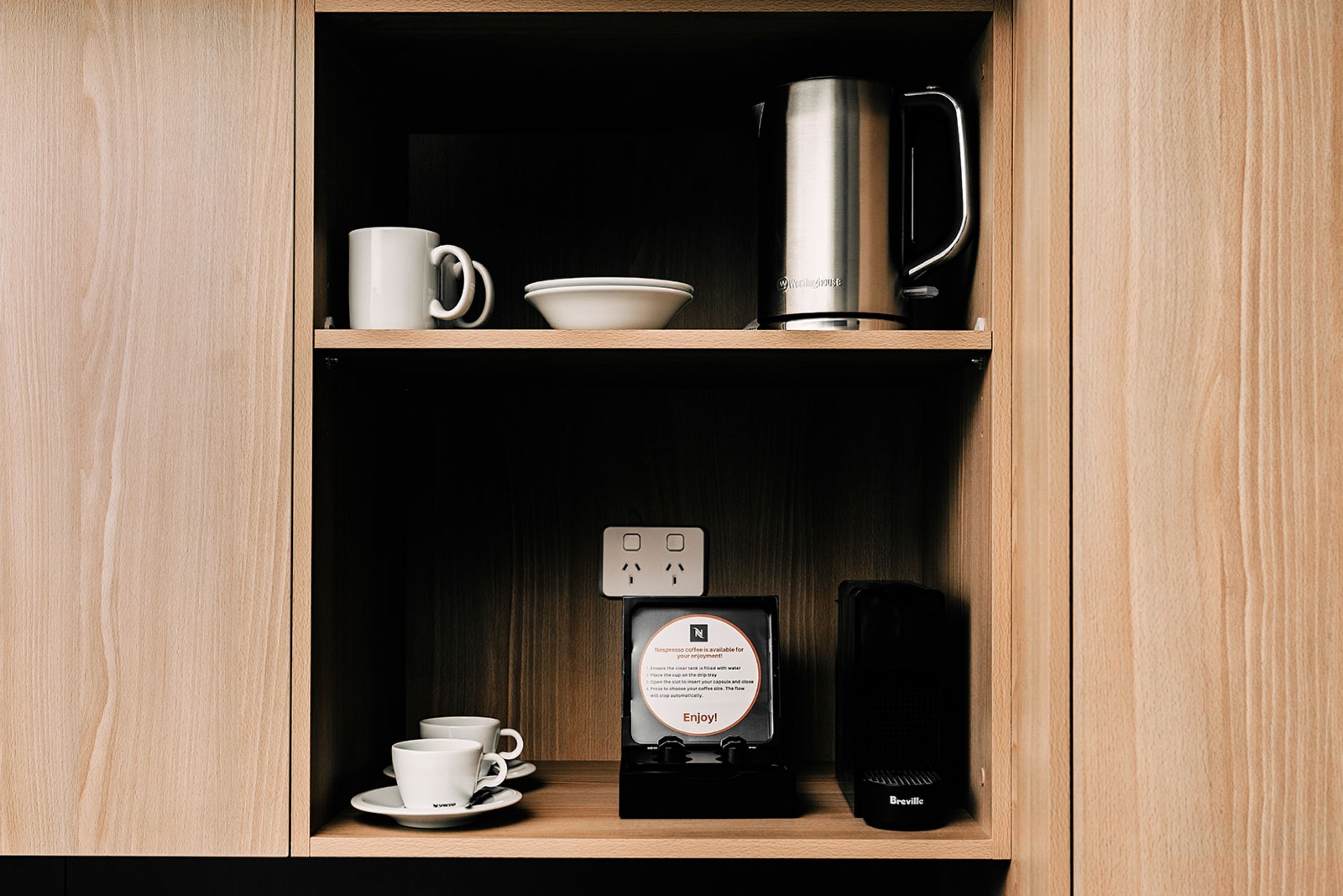 A wooden cabinet with a coffee maker, cups, and a sign.