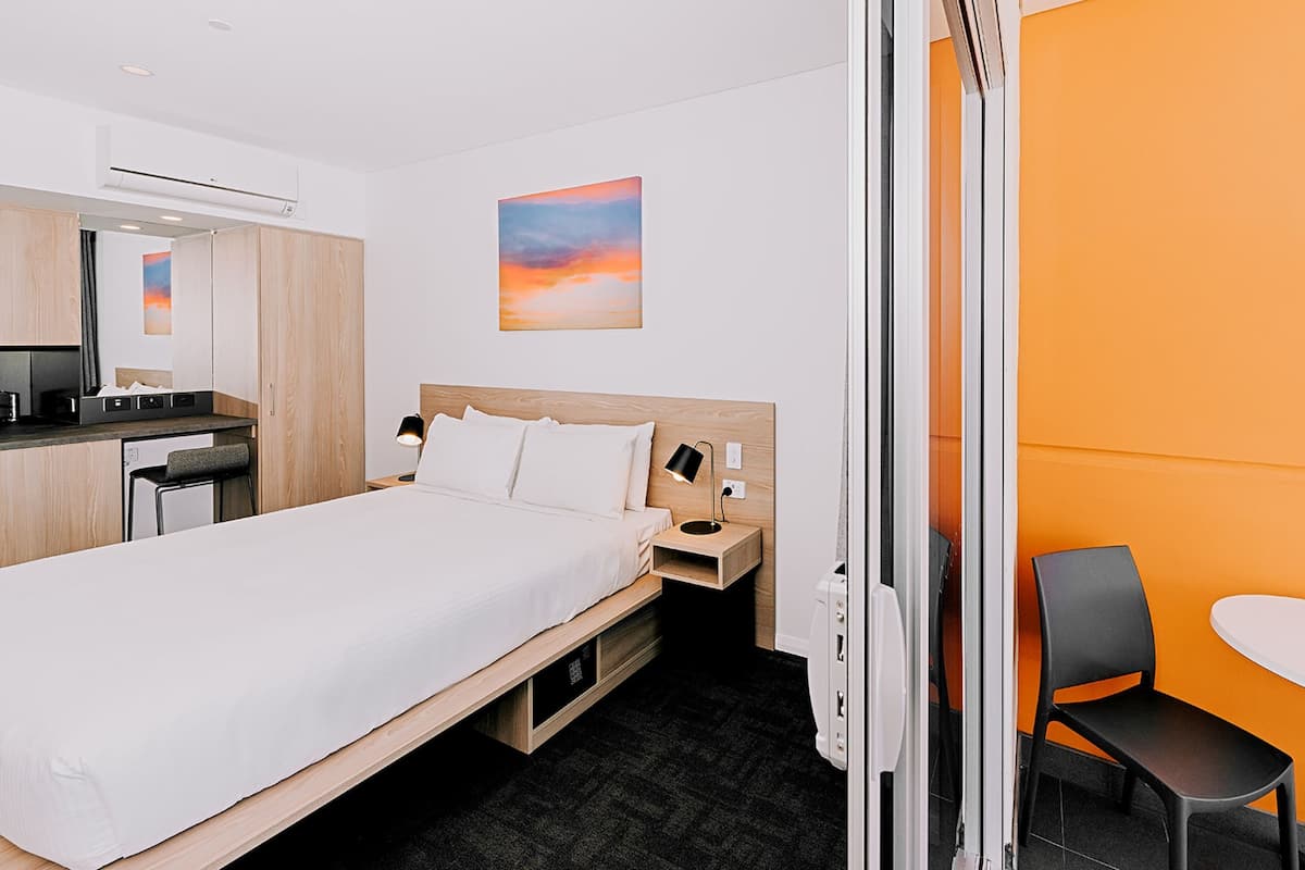 A hotel room with a bed, bedside table, chair, and a small desk area.