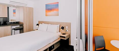 A hotel room with a bed, bedside table, chair, and a small desk area.