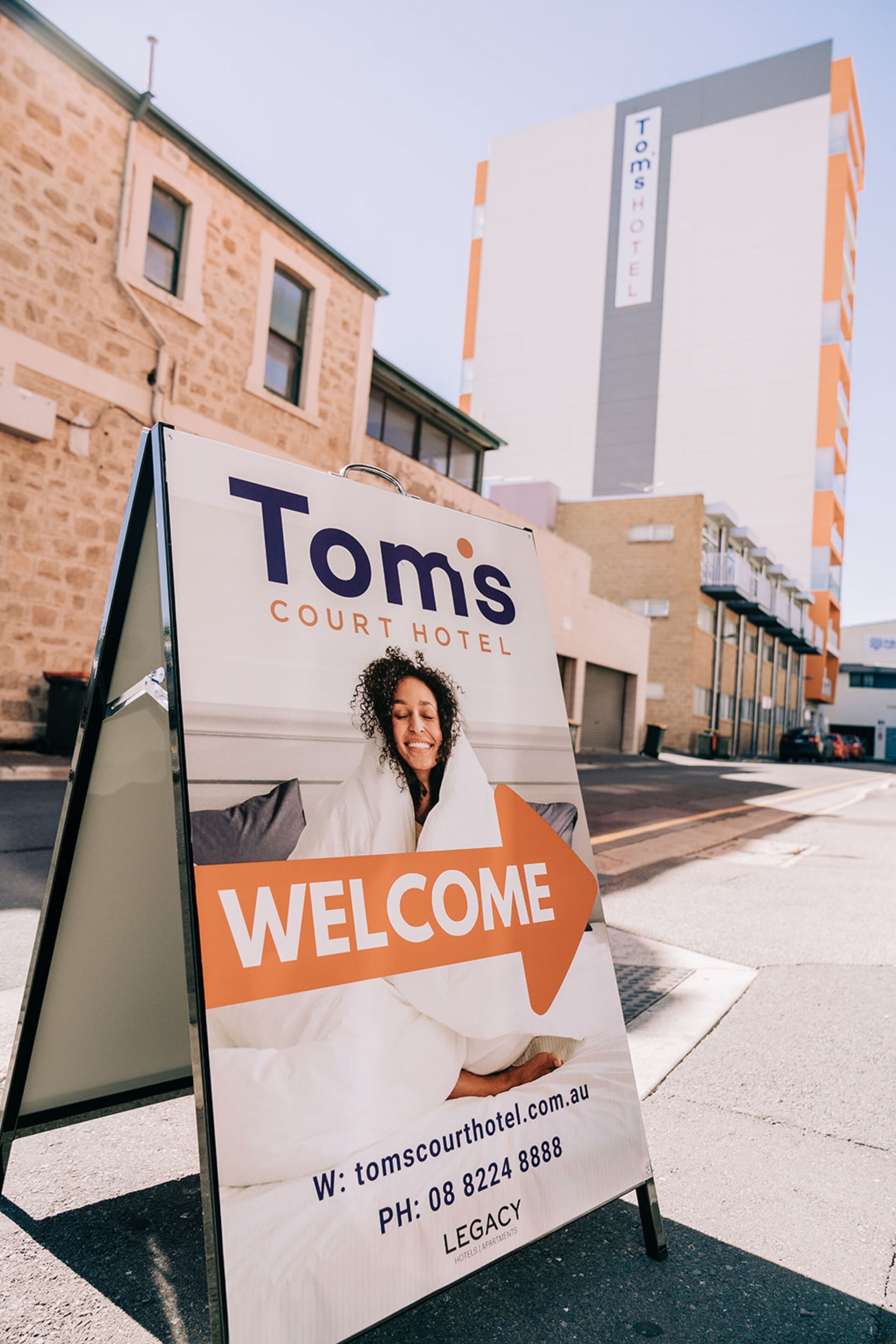 Señal de bienvenida del Hotel Tom's Court con información de contacto y una dirección web.