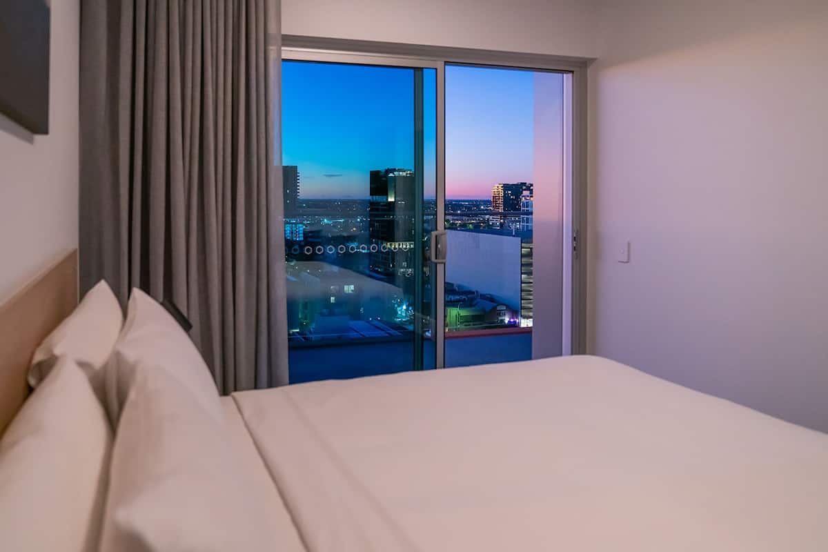 A hotel room with a bed, a view of the cityscape through a sliding door, and a curtain on the left.
