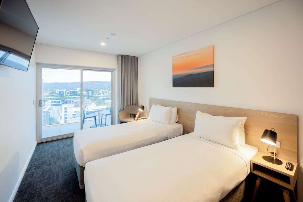 A hotel room with two beds, a desk, a chair, a TV, and a painting.