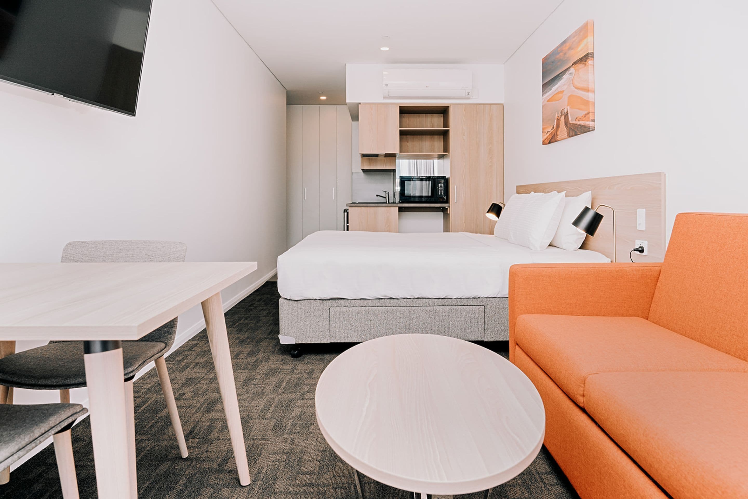 Habitación de hotel compacta con cama, sofá, mesa de comedor y pequeña cocina.