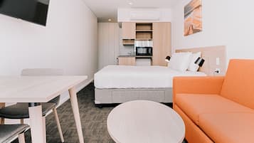 Habitación de hotel compacta con cama, sofá, mesa de comedor y pequeña cocina.