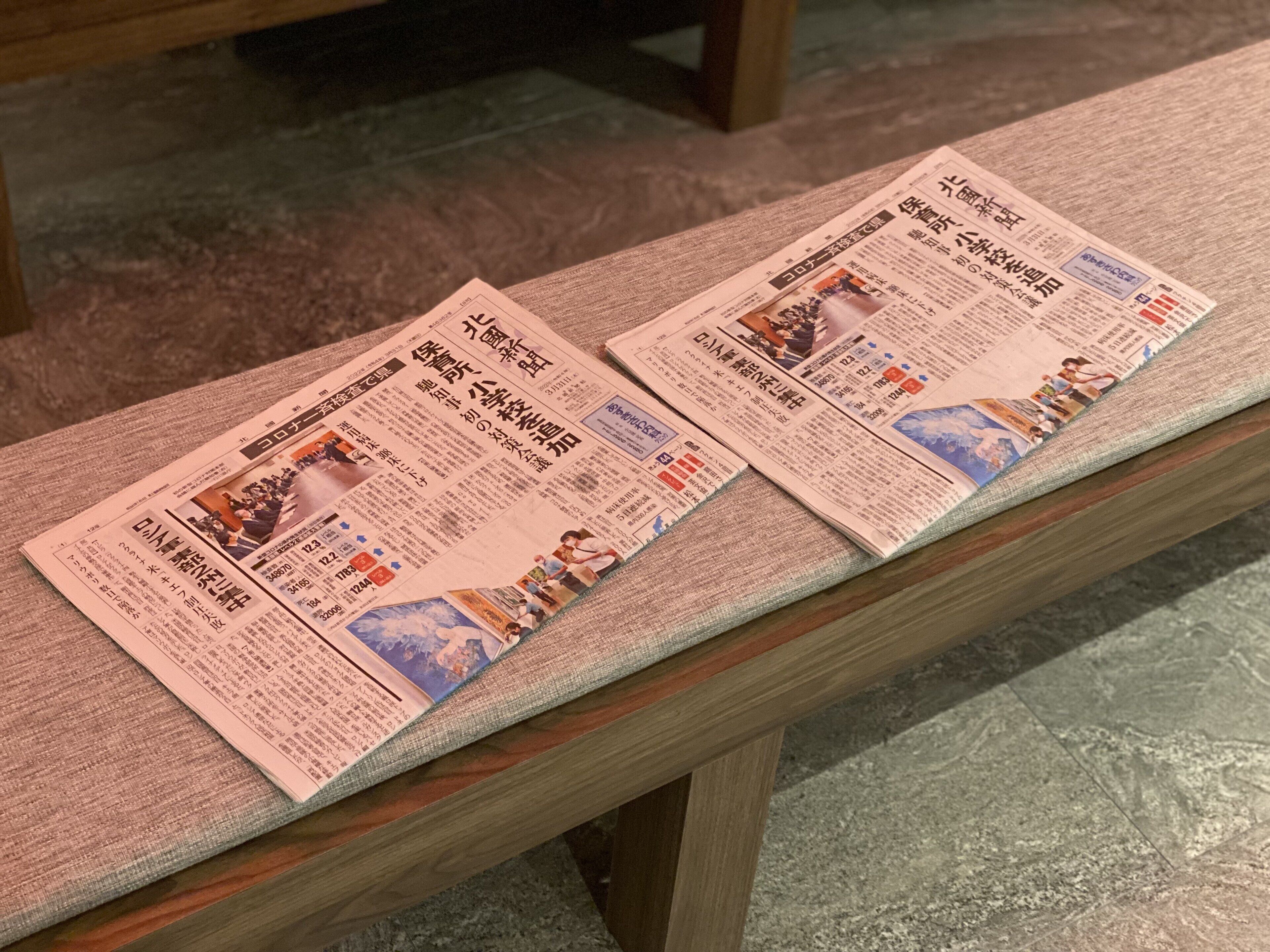 Two newspapers placed on a wooden bench.
