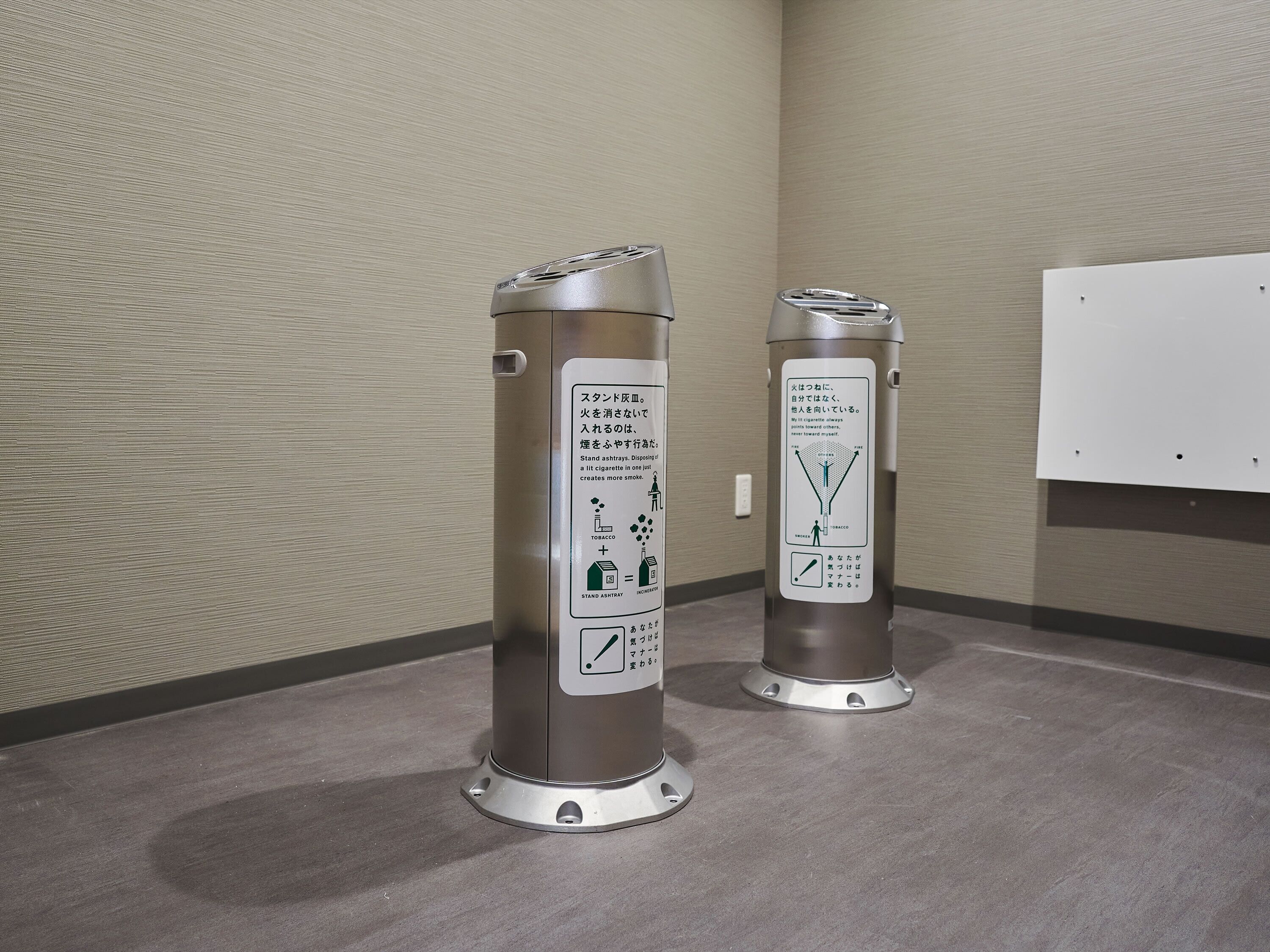 Two trash cans with instructions in Japanese, placed on a grey floor against a textured wall.