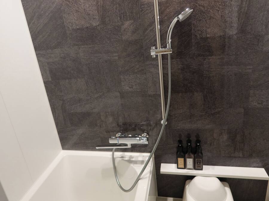 Et moderne badeværelse med badekar, bruser med håndbruser og en hylde med flasker.