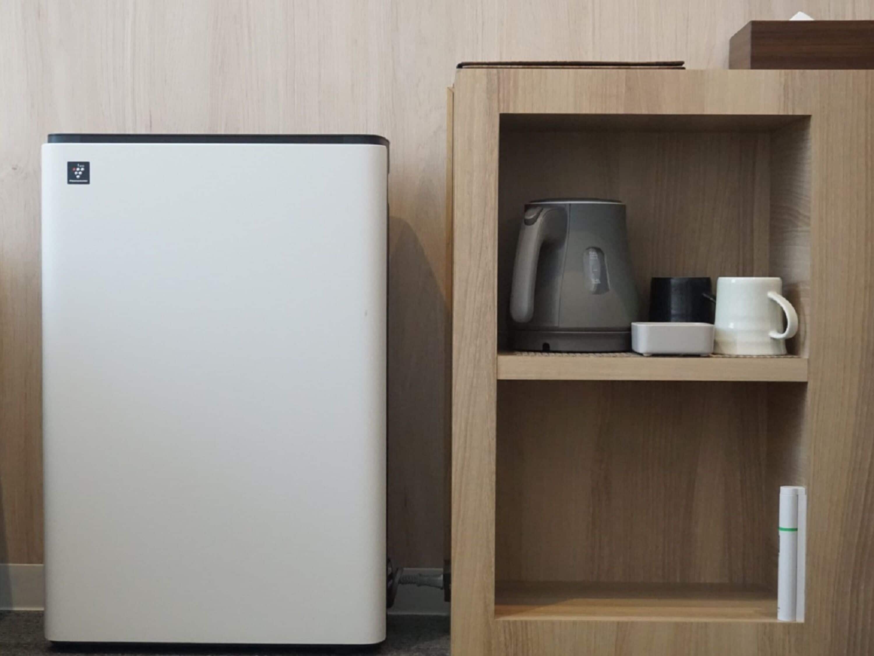A modern kitchen with a white refrigerator, a wooden cabinet with a kettle, a coffee maker, and a mug.