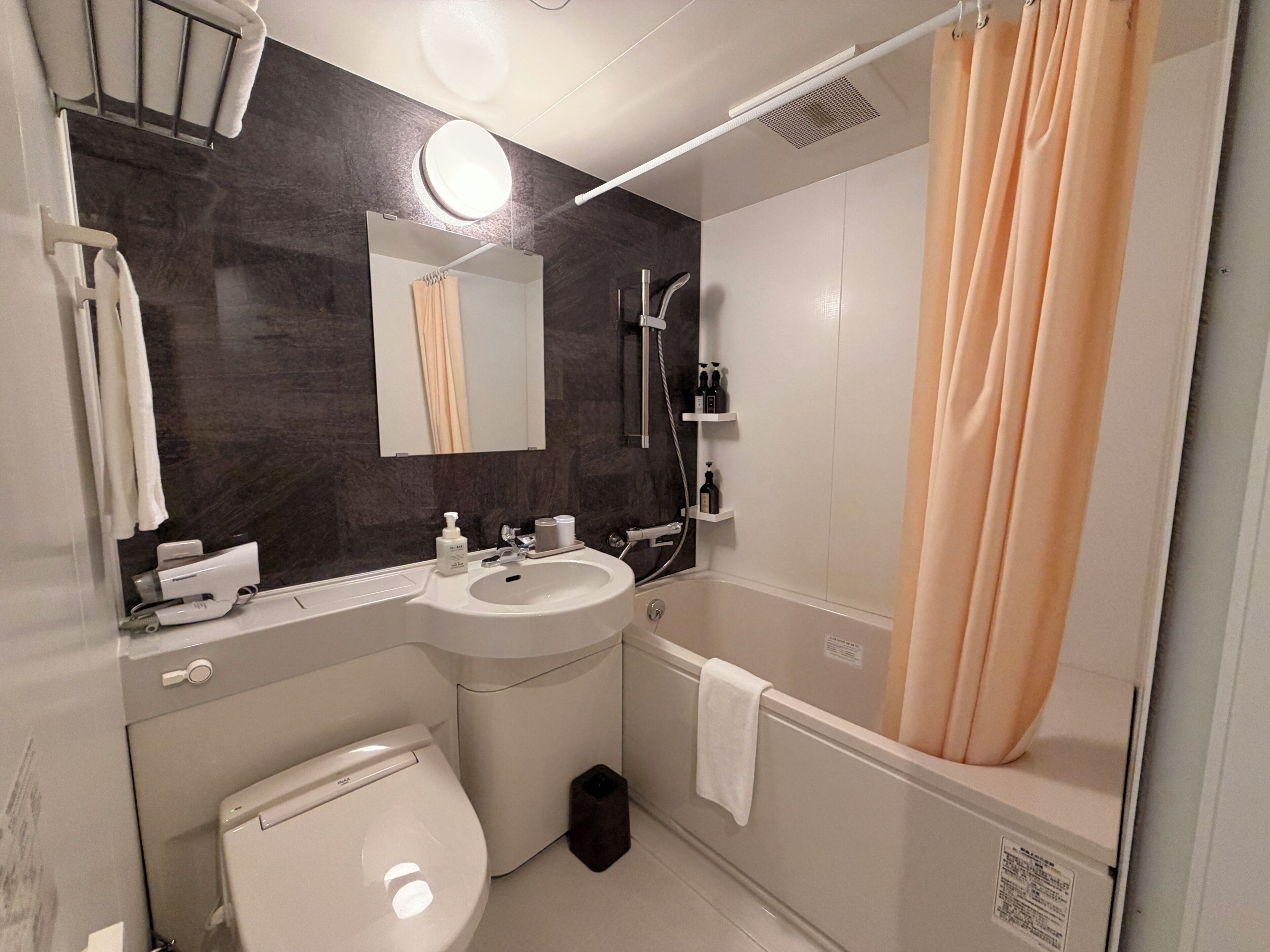 A bathroom with a toilet, sink, mirror, and shower area.