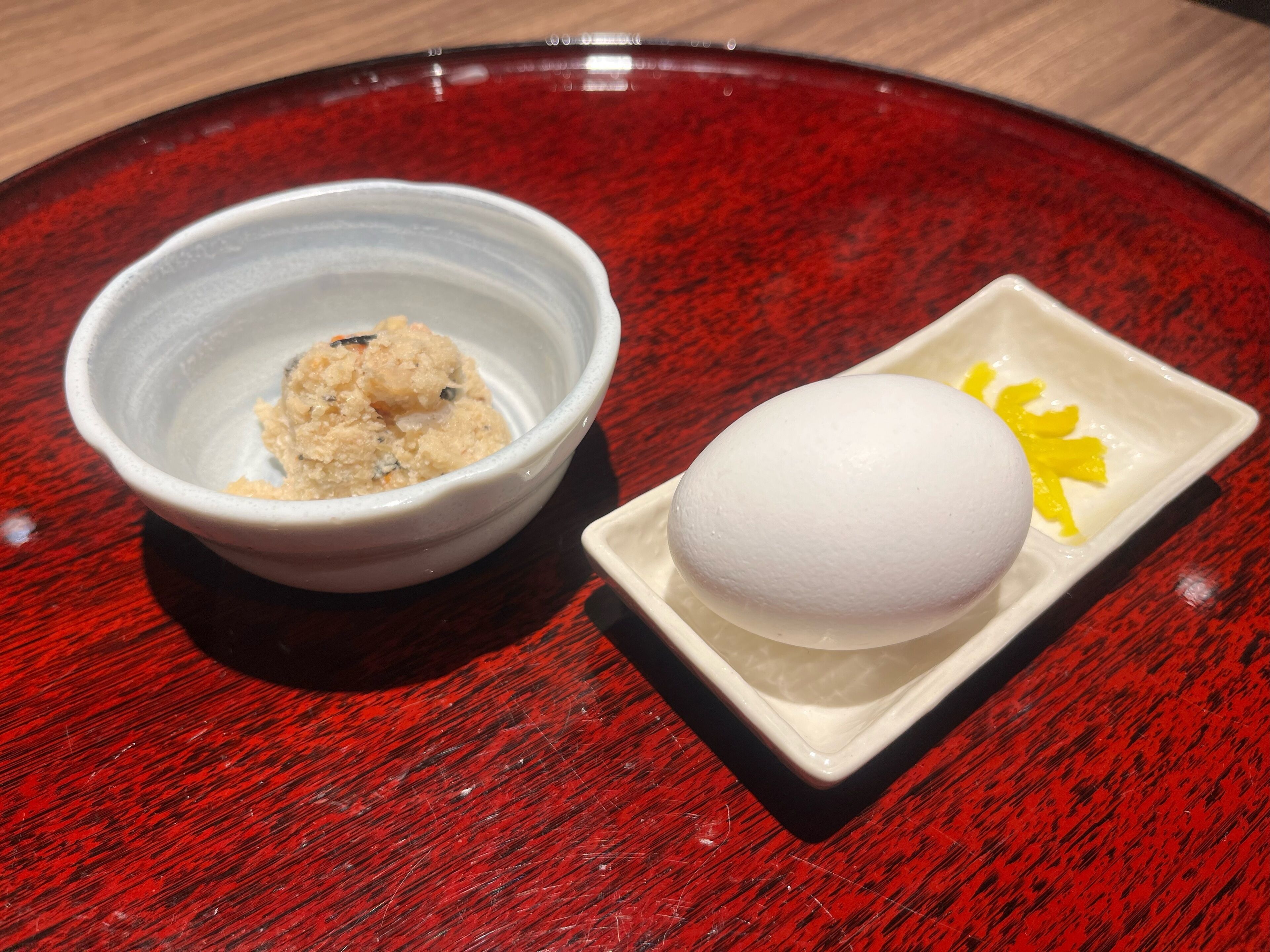 A white bowl with a textured substance and a white spherical object on a red table.