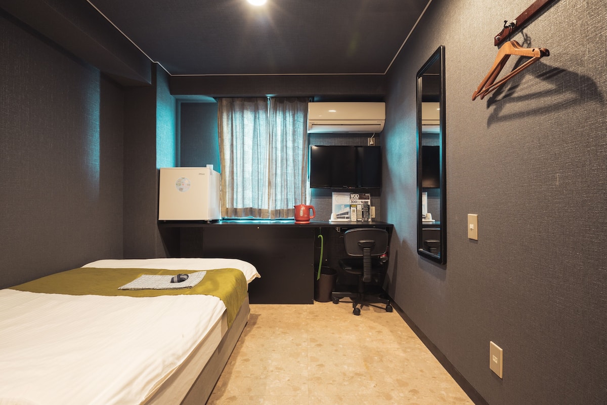Habitación de hotel pequeña con cama, escritorio, silla, televisor y ventana con cortinas.
