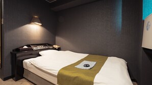A neatly made bed with a white sheet and a green blanket, a bedside table with a lamp, and a wall-mounted phone. - Maruni Hotel Ise (Ise)