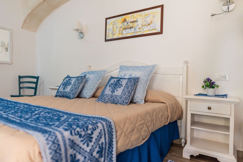 Een slaapkamer met een bed, nachtkastje, stoel en een schilderij aan de muur.