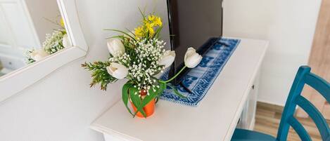 A white desk with a blue patterned placemat, a potted plant with white and yellow flowers, and a blue chair.
