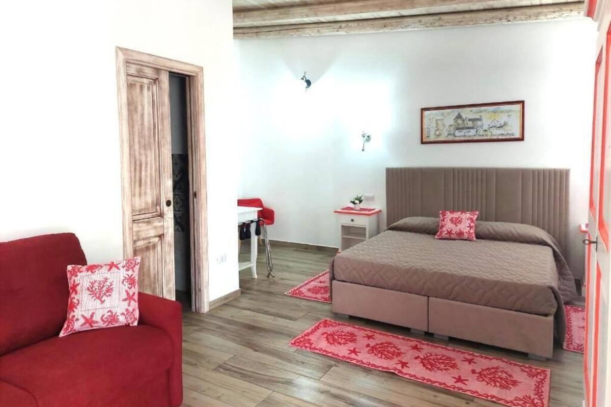 A bedroom with a bed, a red sofa, a wooden ceiling, and a small table with a lamp.