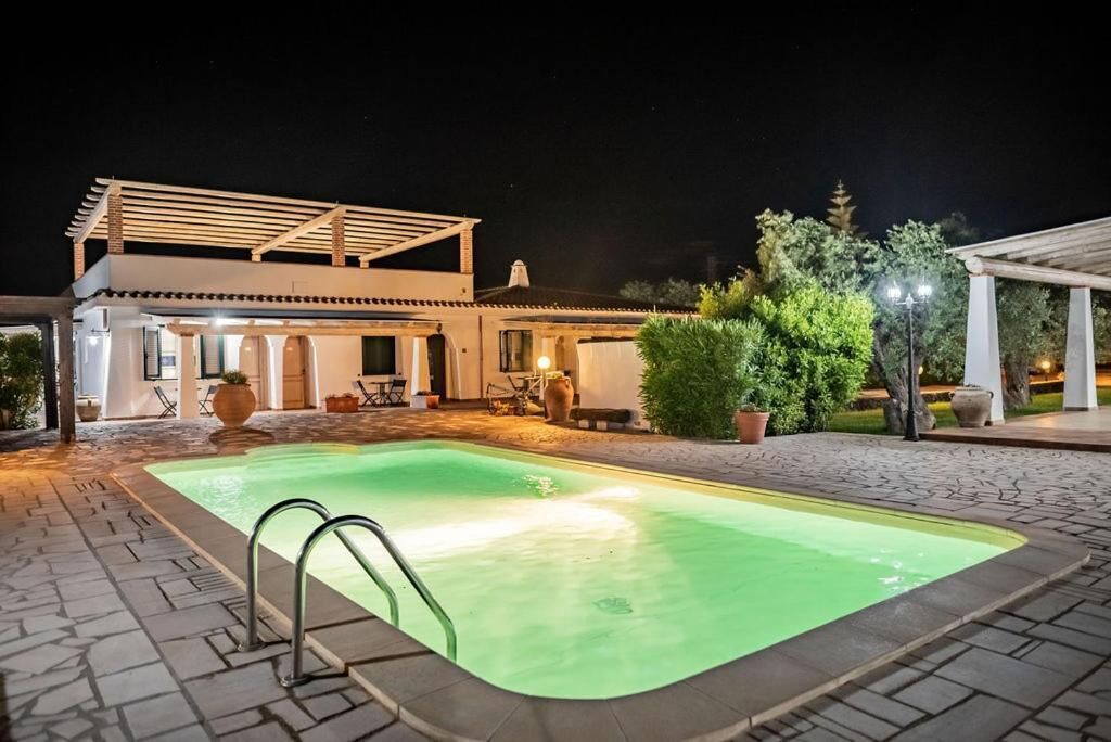 A swimming pool with a pergola, outdoor seating, and a well-lit patio area.