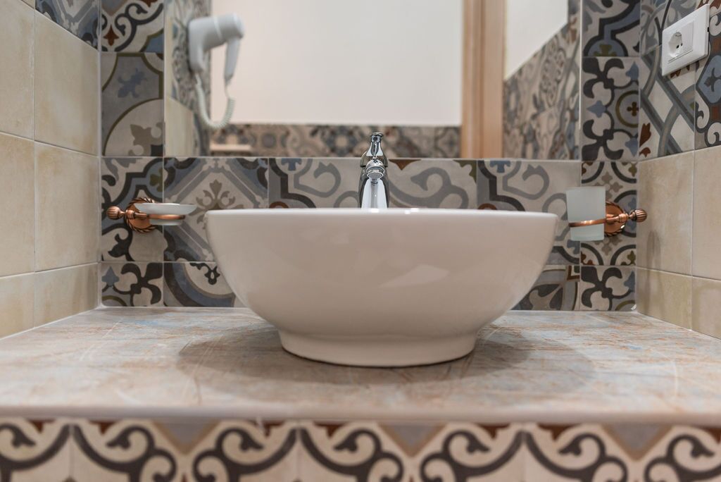 A bathroom with a white basin, patterned tiles, and copper fixtures.