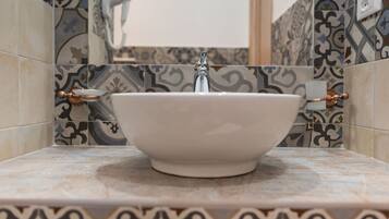 A bathroom with a white basin, patterned tiles, and copper fixtures.