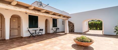 A courtyard with a tiled floor, a large planter, and a building with arches and a wooden pergola.