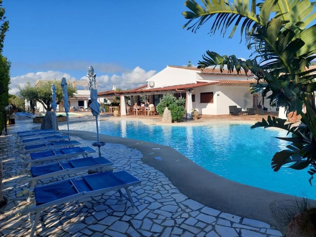 Una piscina con sillones de descanso, un patio y un edificio con techo de tejas.