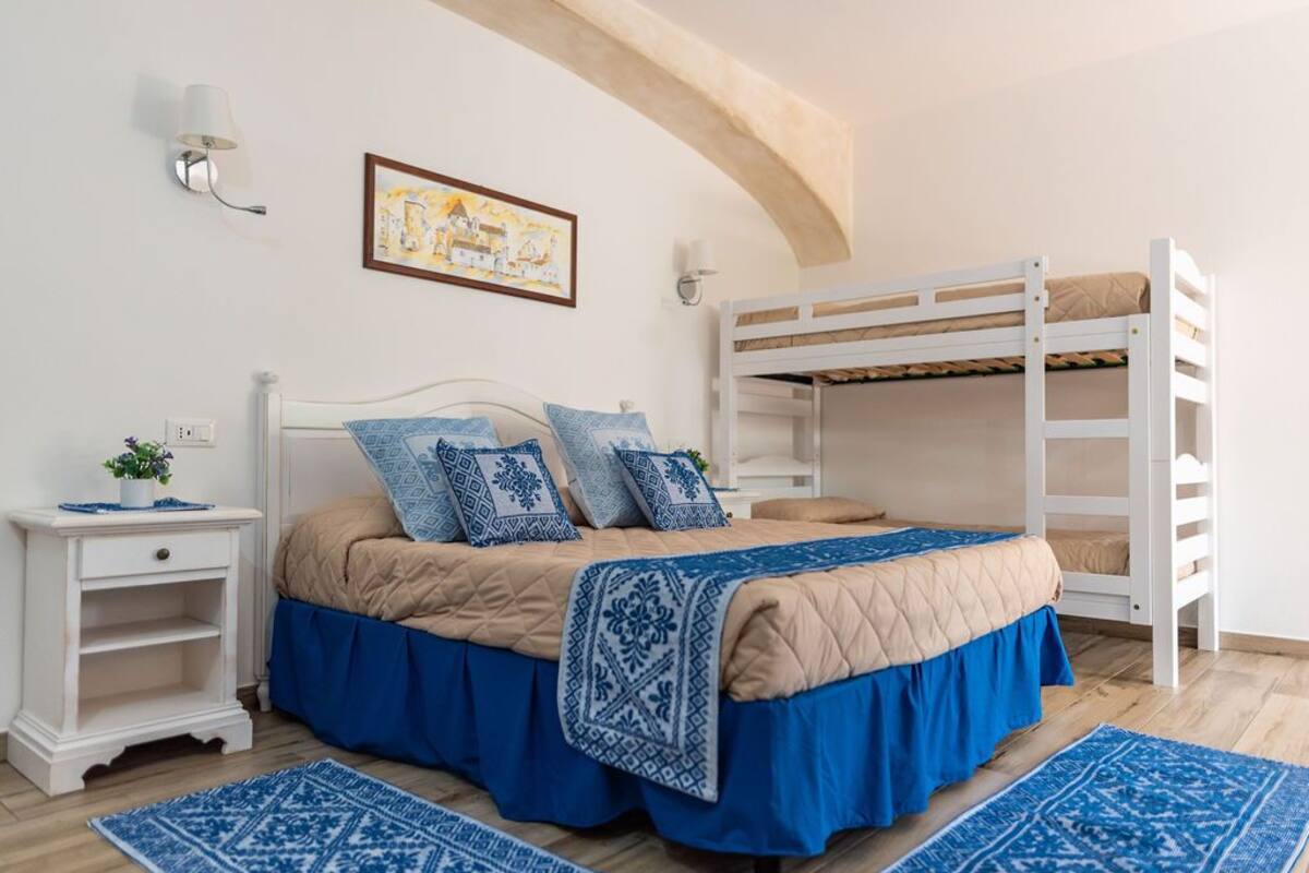 A bedroom with a bunk bed, a bedside table, a lamp, and a framed picture on the wall.