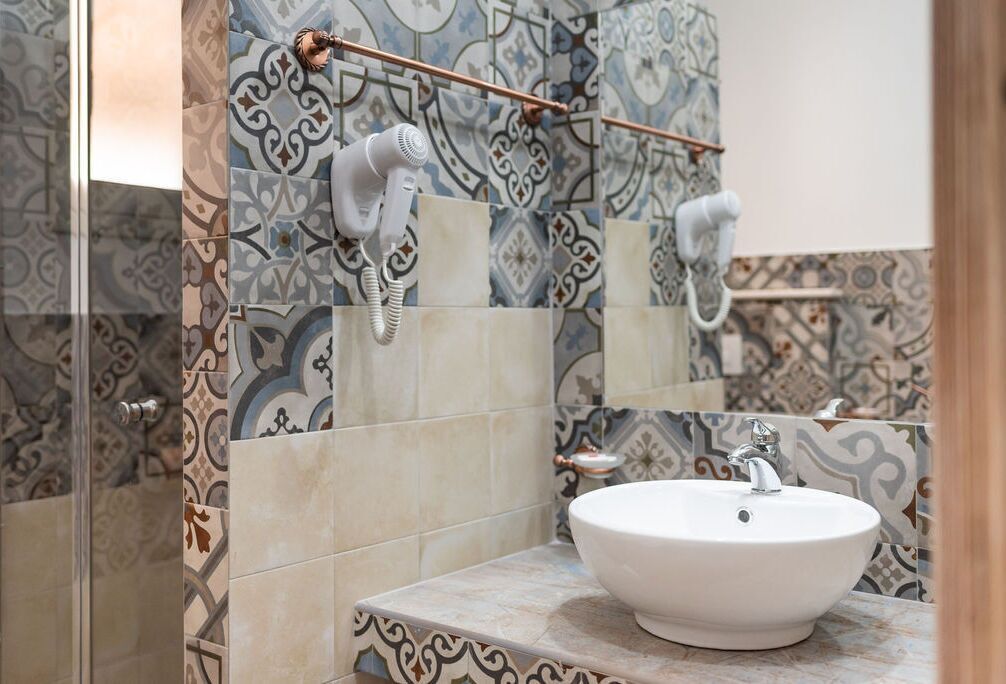 A bathroom with patterned tiles, a white sink, and a hairdryer mounted on the wall.