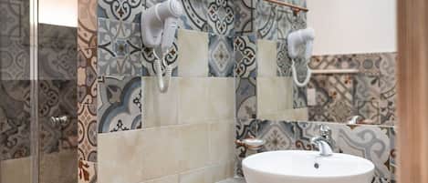 A bathroom with patterned tiles, a white sink, and a hairdryer mounted on the wall.