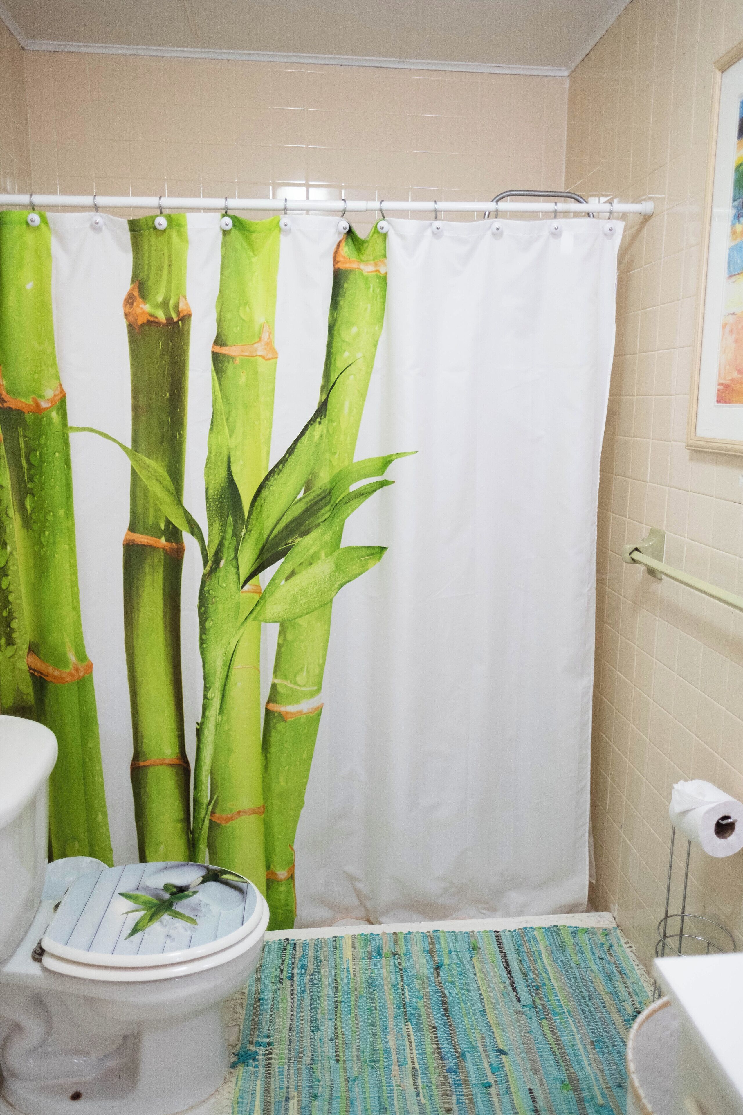 A bathroom with a bamboo-themed shower curtain, a toilet, a patterned rug, and a toilet paper holder.