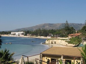 A coastal view with a beach, a building with a tiled roof, and a mountainous background. - Villa Polimia in Full Relaxation - Air-conditioned - Wi-fi (Syracuse)