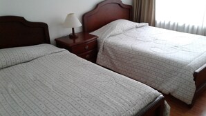 Two single beds with matching floral-patterned bedding, a wooden nightstand with a lamp, and a window with curtains. - The Hostel Bogota Real (Bogotá)