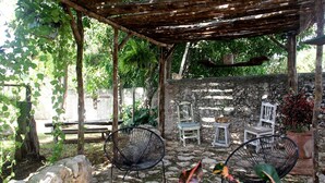 Un área de estar techada al aire libre con paredes de piedra, dos sillas de mimbre y un banco de piedra.