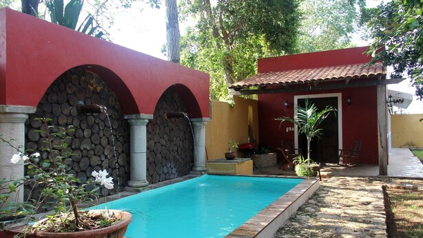 Una piscina con un muro de piedra y un edificio rojo con tejado de baldosas.