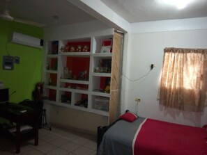A room with a bed, a desk, and shelves with various items.