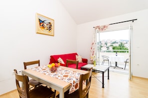 A dining area with a table set for two, a red sofa, and a view of a balcony with a table and chairs.