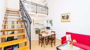 Un apartamento moderno con una escalera de madera, un comedor con mesa y sillas, un sofá rojo y una cocina con armarios blancos.