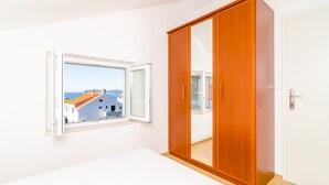 Un dormitorio con un armario grande, una ventana con una persiana abierta y vistas a edificios.