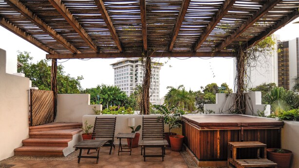 Un espacio al aire libre techado con un jacuzzi, sillas de madera y plantas en macetas.