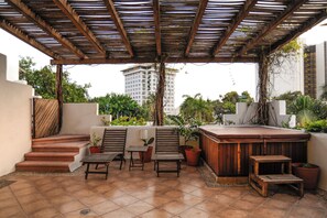 Un espace extérieur abrité comprenant un jacuzzi, des chaises en bois et des plantes en pot.