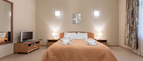 A hotel room with a large bed, a television on a wooden cabinet, two bedside lamps, and a painting on the wall.