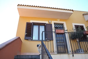A yellow building with a staircase, a metal railing, and a dog on the steps.