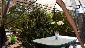 Patio esterno con tavolo e sedie, immerso nel verde e caratterizzato da una struttura pergolata.