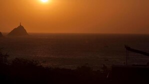 A sunset over the ocean with a silhouette of a mountain and a structure on it. - Apartment in Taganga (Santa Marta)
