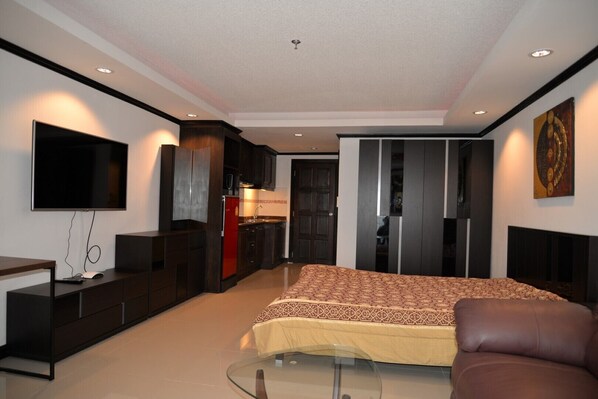 A modern bedroom with a bed, a TV, a desk, and a kitchenette.