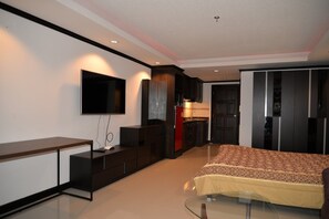 A modern bedroom with a bed, a TV, a desk, and a kitchenette.