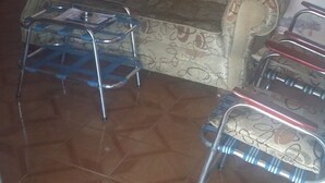A living room with a patterned sofa, a glass coffee table, and a metal folding chair. - The Ancestral Magic of Huila for the Whole World (Neiva)