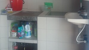 A small kitchen with a sink, a red bucket, and various cleaning supplies on the counter. - The Ancestral Magic of Huila for the Whole World (Neiva)