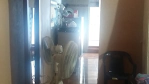 A room with a tiled floor, a standing fan, a plastic chair, and a table cluttered with items. - The Ancestral Magic of Huila for the Whole World (Neiva)
