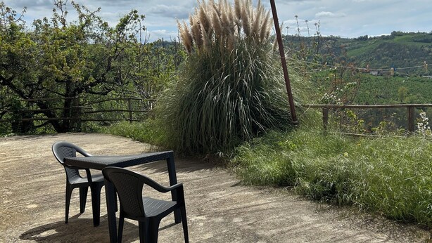 Ein Sitzbereich im Freien mit Tisch und Stühlen, umgeben von Grün und Blick auf eine hügelige Landschaft.