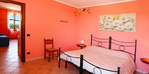 A bedroom with a bed, a chair, a bedside table, a window, and a painting on the wall.
